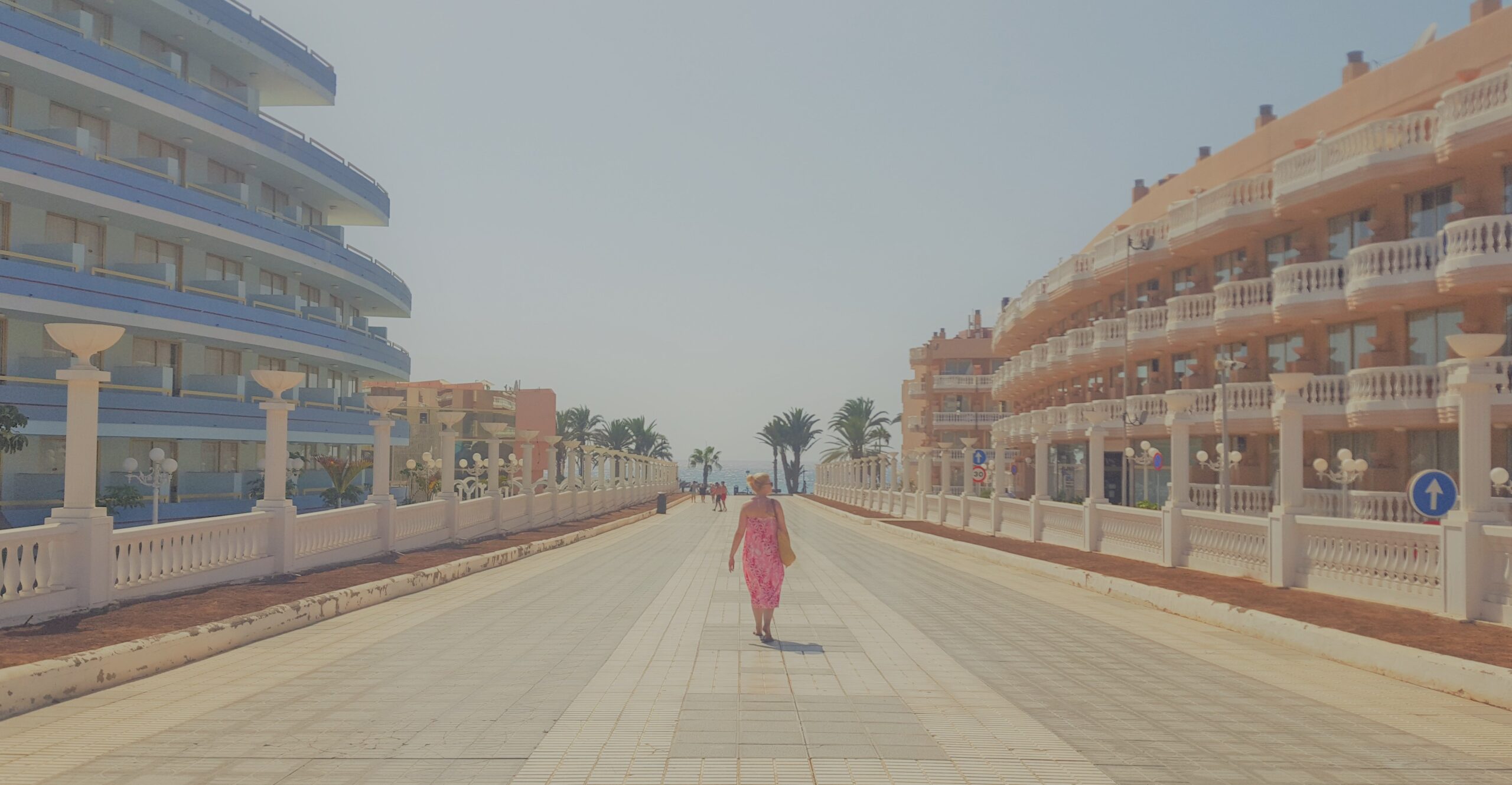 Woman in pink dress walking away down pathway between two hotels
