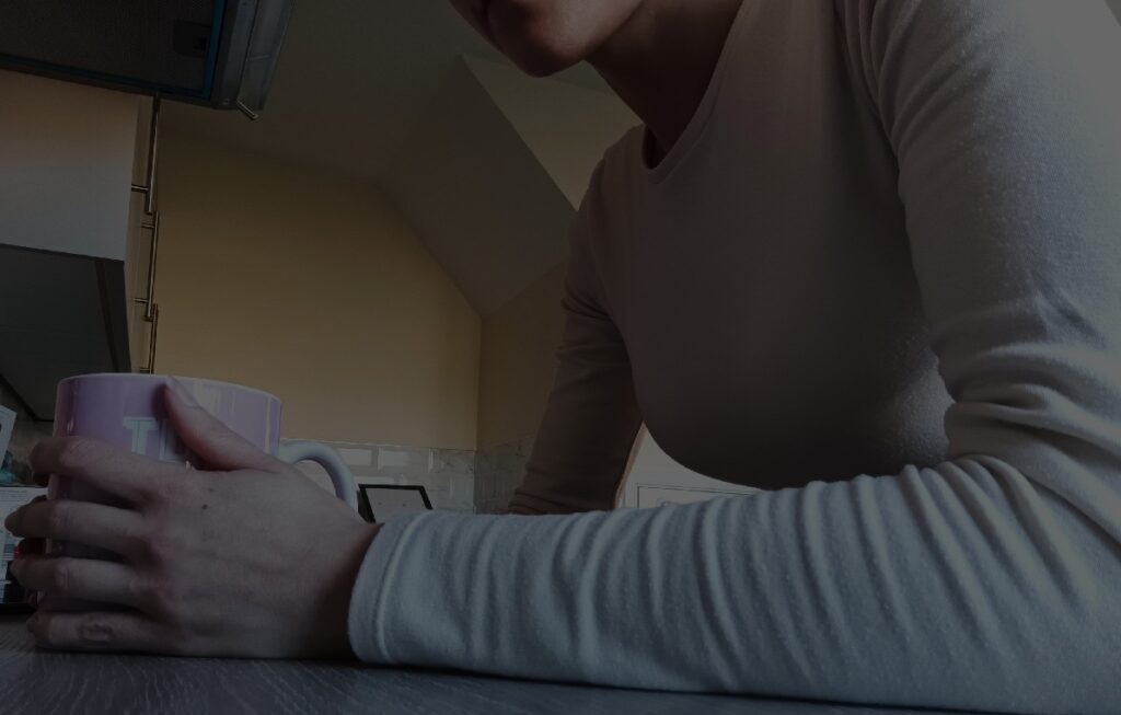 A darkened close up of a woman leaning on a kitchen side holding a mug