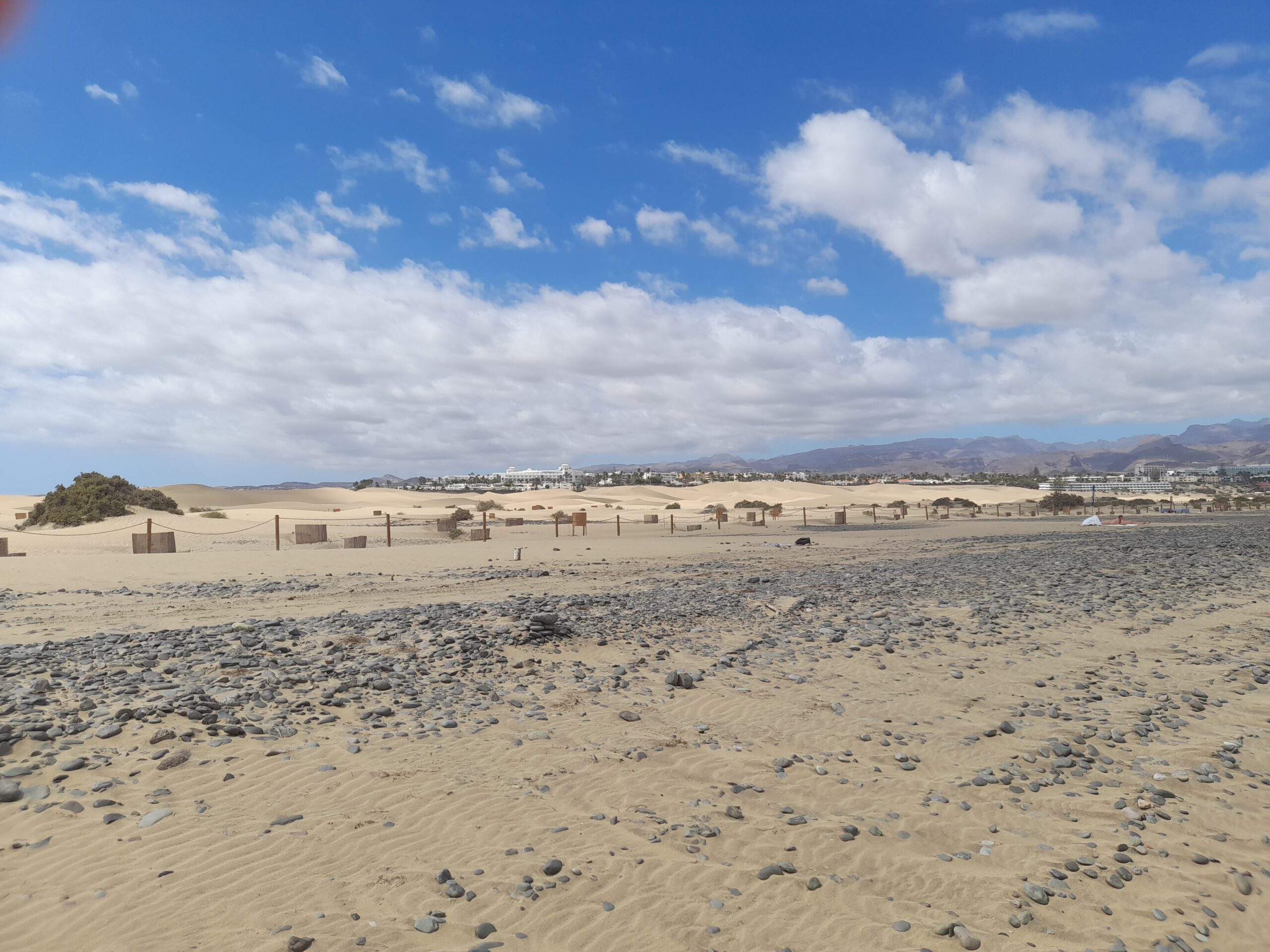Golden sandy beach with some pebbles and a white cloudy blue sky